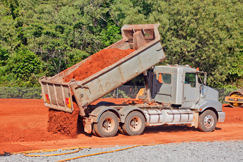 Dump truck emptying red dirt on a construction site. 