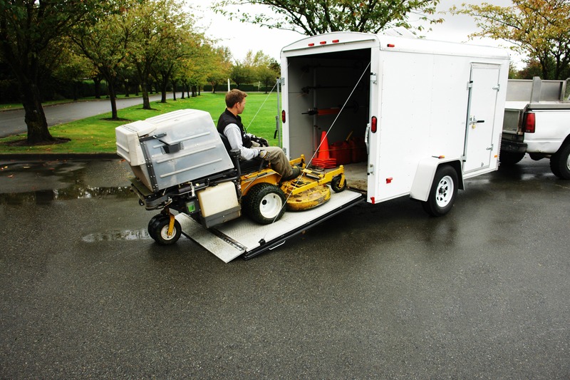 A person rides a lawnmower into an enclosed trailer.